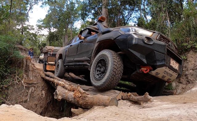 A performance enhanced 4x4 is driving over a log in the woods while off-roading.