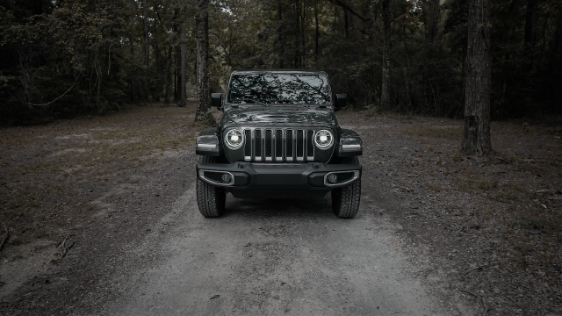 A black jeep parked on a dirt road in the woods.