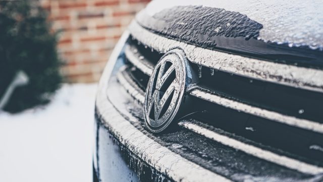A black Volkswagon is parked in the snow, possibly in need of winter car servicing.