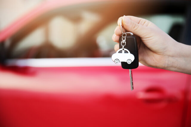 A person holding a car key in front of a red car, contemplating whether cars make good Christmas gifts.
