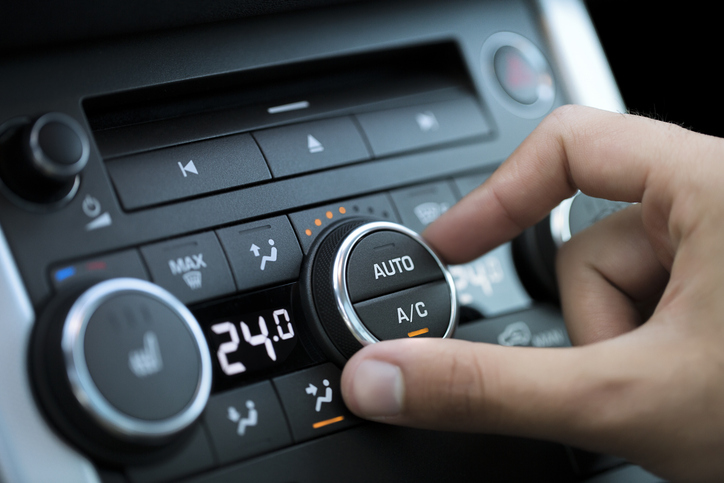 A hand is adjusting the automatic air conditioning control knob in a car, with the temperature set to 24 degrees Celsius, ensuring you stay cool in summer.