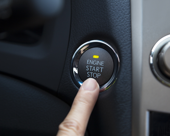 A finger pressing an illuminated "Engine Start Stop" button on a car dashboard, highlighting potential starting issues.