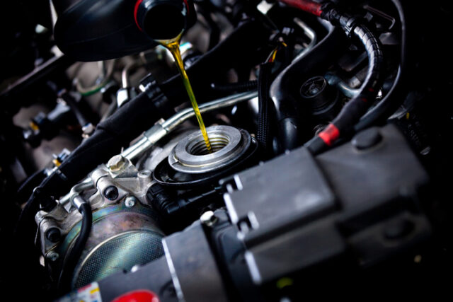 Close-up of motor oil being poured into a diesel engine's oil reservoir from a bottle. Various engine components and cables are visible surrounding the filling process, showcasing best practices for maintaining your vehicle.