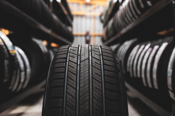 A close-up view of a new car tyre on display in a warehouse, surrounded by shelves filled with more tyres.