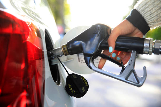 A person fills a European vehicle with diesel fuel at a gas station, holding a diesel pump nozzle inserted into the tank to support fuel efficiency on the road.