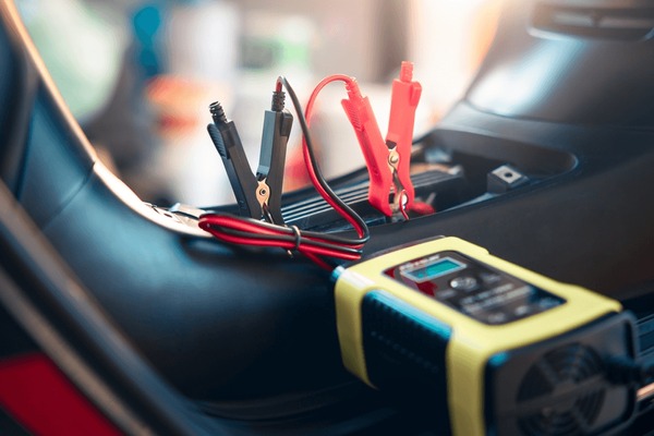 A portable car battery charger with attached red and black jumper cables is connected inside a vehicle—perfect to ensure you can store your European car safely without worrying about a dead battery.